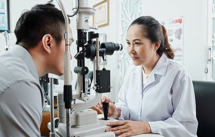 Asian female optometrist looking through the special medical equipment and examining her patient's eyesight at hospital