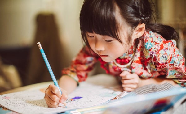 Lovely little girl in traditional Chinese costumes concentrate on colouring a colouring book happily.