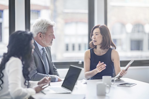 Businesswoman discussing with colleagues. Entrepreneurs are planning in board room. They are sitting at table in office.