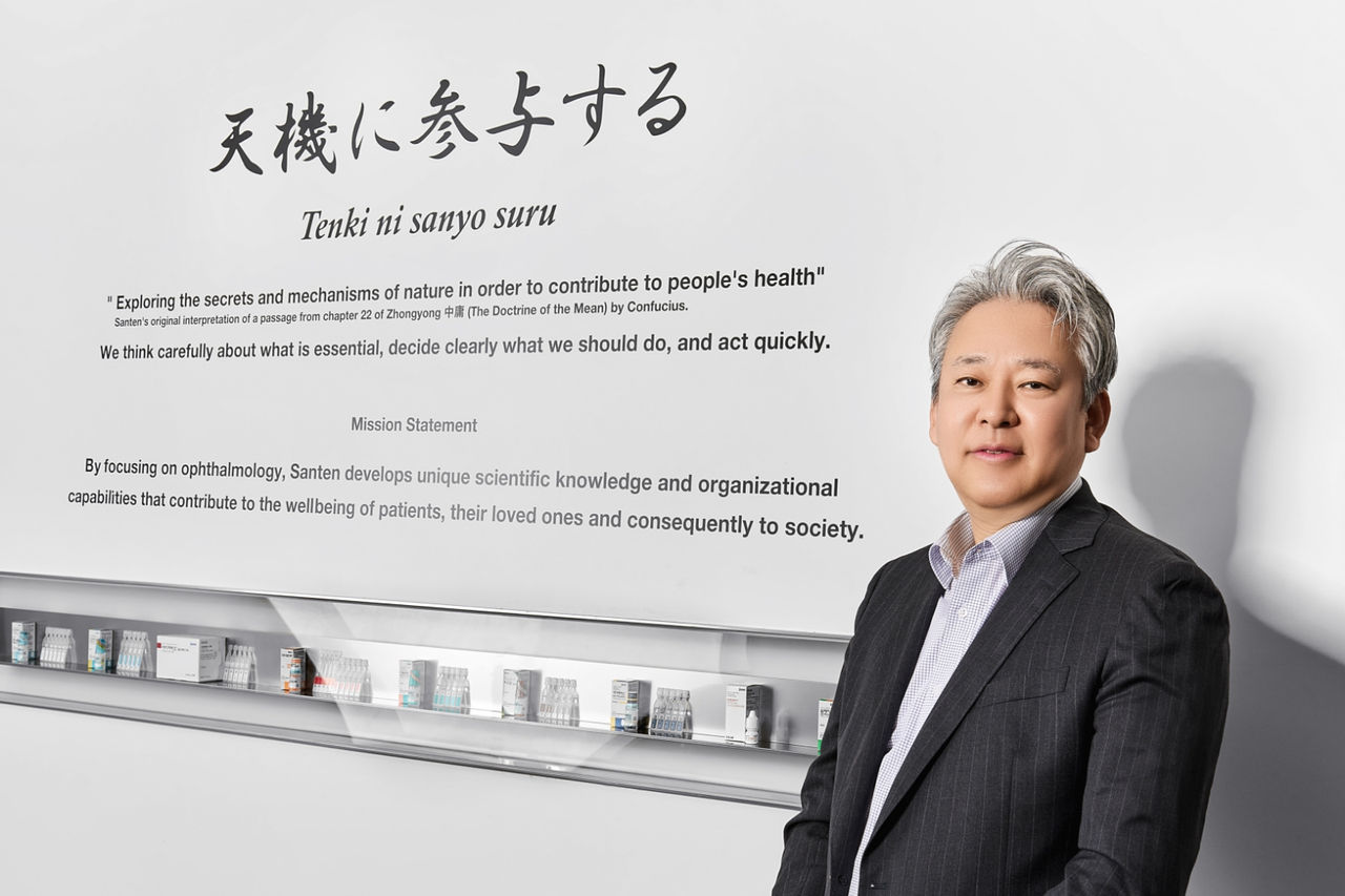 Photo of Lee Han-Woong standing in front of a wall displaying Santen’s Corporate Philosophy