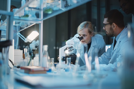 Medical Development Laboratory: Team of Female and Male Scientist Using Microscope, Analyzes Petri Dish Sample. Specialists Working on Medicine, Biotechnology Research in Advanced Pharma Lab