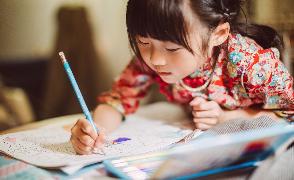 Lovely little girl in traditional Chinese costumes concentrate on colouring a colouring book happily.