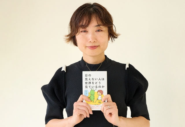 書籍『目の見えない人は世界をどう見ているのか』を胸の前で持つ伊藤教授の写真