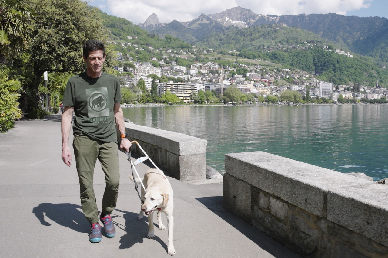 盲導犬と水辺を歩くローランドさんの写真