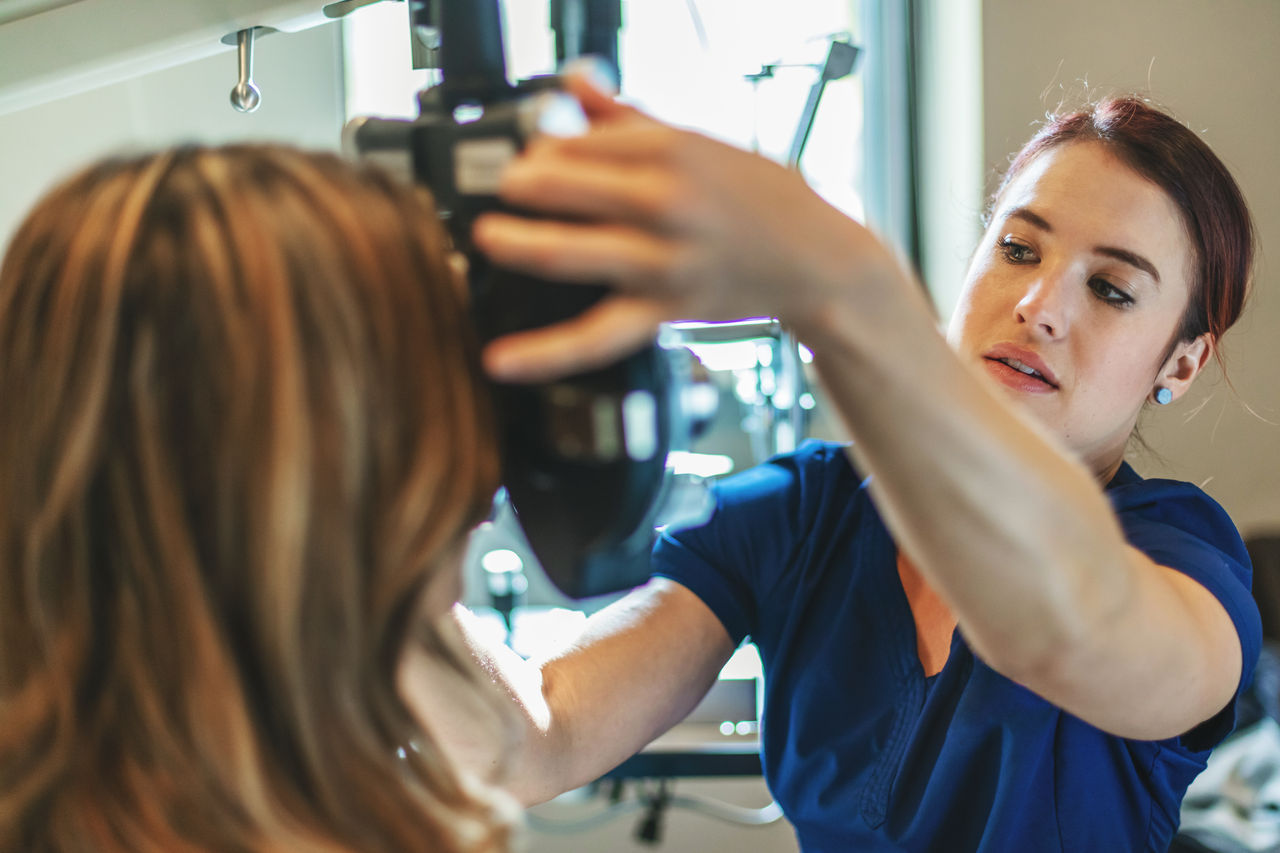 In Western Colorado Eyecare Professional using high tech equipment in eyecare clinic setting part of series with millennial male and female patient (Shot with Canon 5DS 50.6mp photos professionally retouched - Lightroom / Photoshop - original size 5792 x 8688 downsampled as needed for clarity and select focus used for dramatic effect)